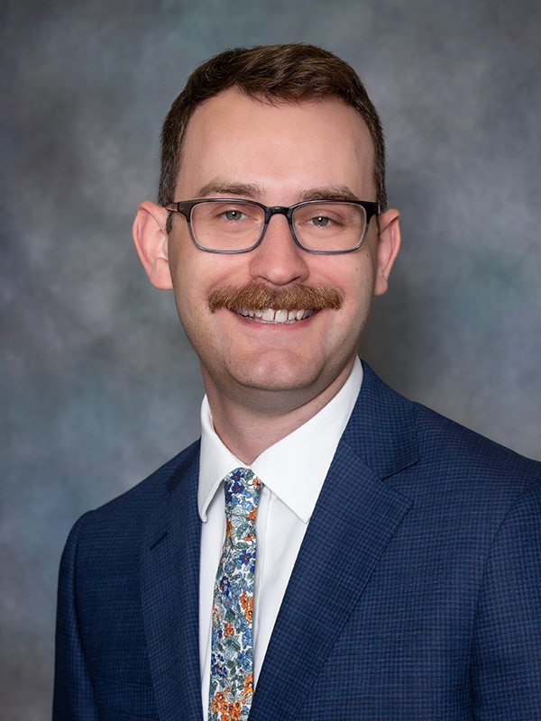 Headshot of Thomas Reuter, pediatrician at South Lake Pediatrics. Thomas is wearing a navy blue suit, has brown hair and glasses, and is smiling at the camera.